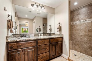 A bathroom with a granite countertop, wooden vanity, a large mirror, and a shower area.