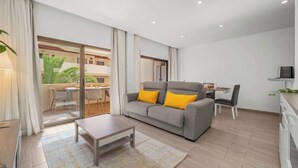 A modern living room with a grey sofa, yellow cushions, a wooden coffee table, and a glass door leading to an outdoor area.