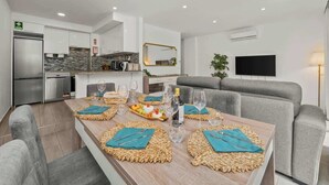 A modern dining area with a long table set for six, surrounded by grey sofas.