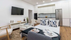 Moderni hotellihuone, jossa on sänky, työpöytä, televisio, pieni keittiö ja kylpyhuone.