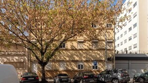 Un espace de stationnement avec plusieurs voitures, un arbre et un bâtiment doté de nombreuses fenêtres et de balcons.