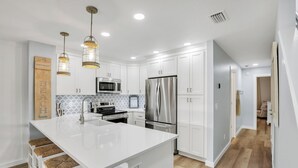 A modern kitchen with white cabinets, stainless steel appliances, and a central island with bar stools. - Drift Away in our cozy coastal retreat in St. Augustine Beach! (St. Augustine)