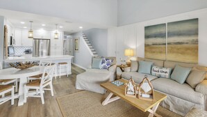 A spacious living room with a large sofa, a coffee table, and a dining area with a white table and chairs. - Drift Away in our cozy coastal retreat in St. Augustine Beach! (St. Augustine)