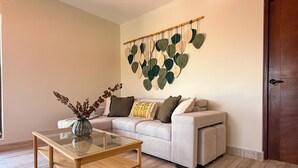 Un soggiorno con un tavolino in vetro, un divano color beige con cuscini decorati e un pannello decorativo a forma di foglia.