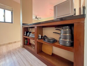 A kitchen with wooden shelves, a microwave, a ceiling fan, and various kitchen utensils.