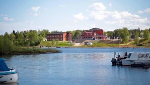 A calm river with boats docked, a red building, and a forested area in the background. - Inari Hotel (Inari)