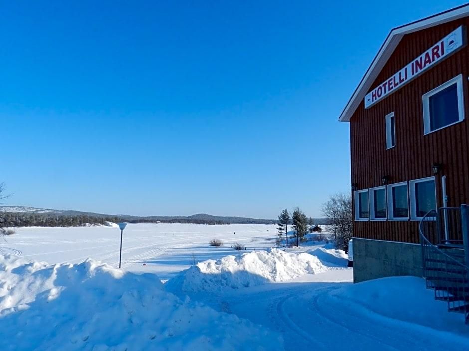 Un hotel llamado "HOTELLI INARI" con fachada de madera, un cielo azul claro y un paisaje nevado al fondo.