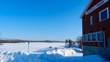 Un hotel llamado "HOTELLI INARI" con fachada de madera, un cielo azul claro y un paisaje nevado al fondo.