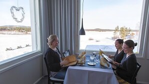 Une table à manger recouverte d’une nappe blanche, des chaises et, par la fenêtre, une vue sur un paysage enneigé.