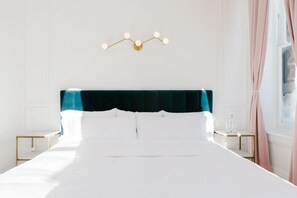 A neatly made bed with white linens, a teal upholstered headboard, and a wall-mounted light fixture. - The Wyman Hotel & Inn (Silverton)