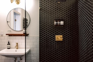 A bathroom with a white sink, a round mirror, and a black hexagonal wall design.