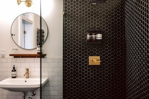 A bathroom with a white sink, a round mirror, and a black hexagonal wall design.