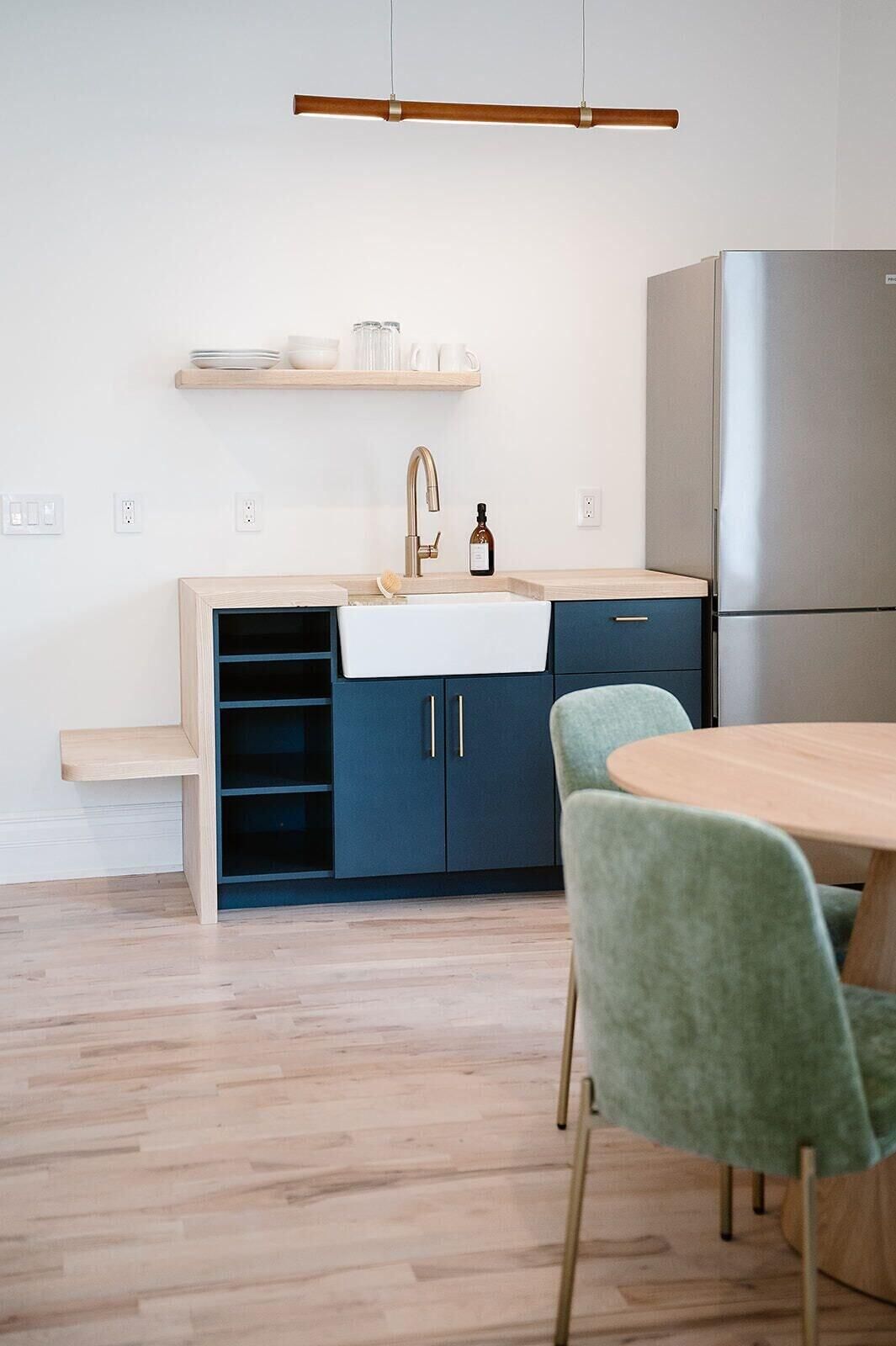 A modern kitchen with a built-in sink, a stainless steel refrigerator, and a wooden dining table with green chairs.