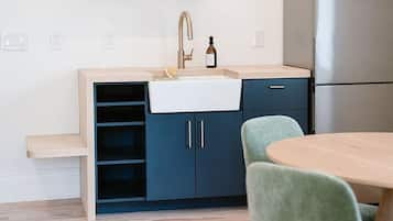 A modern kitchen with a built-in sink, a stainless steel refrigerator, and a wooden dining table with green chairs.