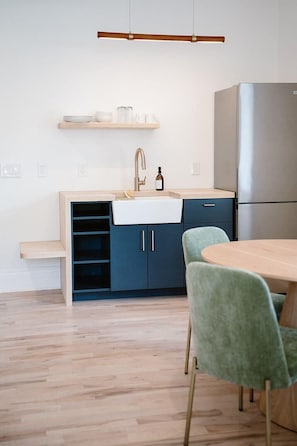 A modern kitchen with a built-in sink, a stainless steel refrigerator, and a wooden dining table with green chairs.