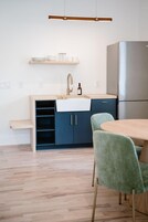 A modern kitchen with a built-in sink, a stainless steel refrigerator, and a wooden dining table with green chairs.