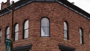 Un bâtiment en briques doté de fenêtres en arc de cercle et d’une grande porte, une enseigne indiquant « Bienvenue à Silverton », et un hydrant rouge sur le trottoir.