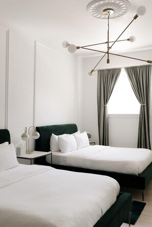 Une chambre d’hôtel moderne avec deux lits, une tête de lit verte, une table de chevet avec une lampe et un luminaire au plafond.