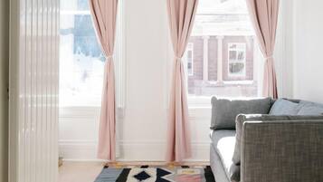 A modern living room with a grey sofa, a patterned rug, and pink curtains.