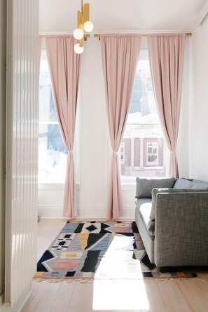 A modern living room with a grey sofa, a patterned rug, and pink curtains. - The Wyman Hotel & Inn (Silverton)