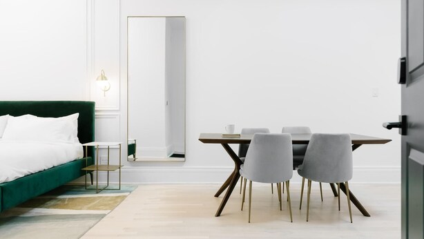 Une pièce moderne avec un canapé vert, une table à manger et quatre chaises, ainsi qu’un grand miroir.