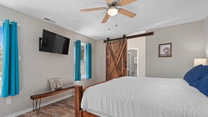 Ein Schlafzimmer mit einem hölzernen Bett, Deckenventilator, einem an der Wand montierten Fernseher und einer Schiebetür im Bauernhausstil.