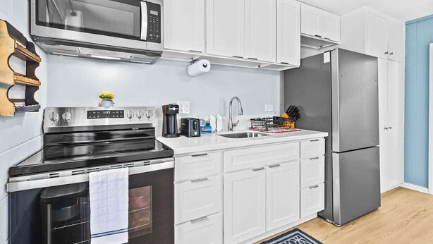 A modern kitchen with white cabinets, a stainless steel refrigerator, a microwave, and a stove. - Aloha Comfort Stay one bedroom with private patio (Honolulu)