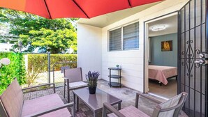 A patio with outdoor furniture, a red umbrella, and a view of a bedroom with a bed and a small table. - Aloha Comfort Stay one bedroom with private patio (Honolulu)