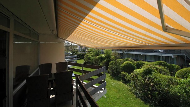 Un balcon agrémenté de mobilier d’extérieur, d’un auvent à rayures et d’un espace végétal bien entretenu.