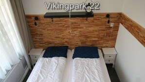 Un lit double avec une literie blanche, une tête de lit en bois, une petite table de chevet et une horloge fixée au mur.