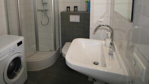Une salle de bain avec une douche à parois de verre, un lavabo et un lave-linge.