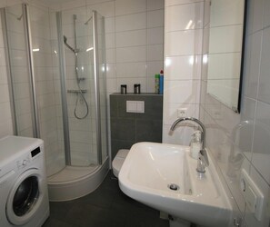 Un baño con ducha de vidrio, lavamanos y lavadora.
