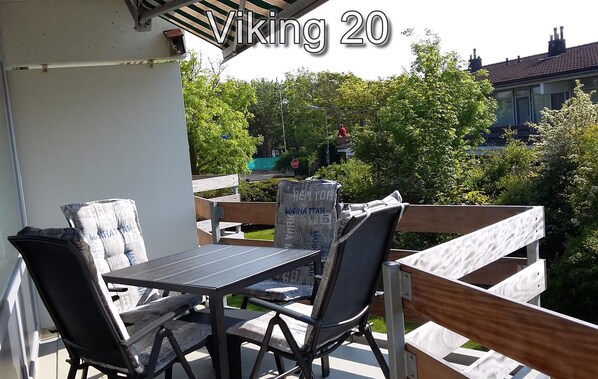An outdoor patio with a table and chairs, a covered area, and a view of greenery and buildings in the background.
