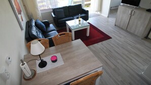 Un salon avec un canapé noir, une table à manger avec des chaises, un téléviseur et un coin cuisine avec un meuble.