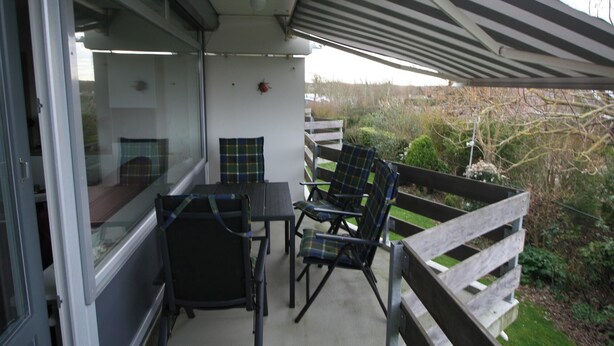 Ein Balkon mit Tisch und Stühlen, Blick auf den Garten und ein roter Käfer an der Wand.