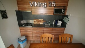A compact kitchen with wooden cabinets, a microwave, a gas stove, and a dining table with chairs. - Comfort Vikingpark 25 (Westkapelle)