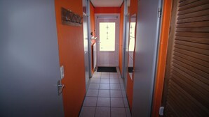 A narrow hallway with orange walls, a tiled floor, and a door at the end.