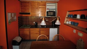 A compact kitchen with wooden cabinets, a microwave, a stove, and a dining table with chairs.