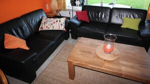 A black leather sofa with colorful pillows, a wooden coffee table with a candle, and a woven placemat.