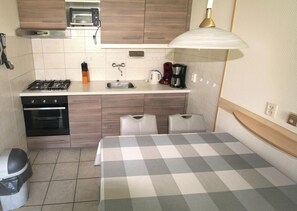 A compact kitchen with a microwave, stove, sink, and a table with a checkered tablecloth.