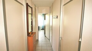Un corridoio stretto con una cassettiera in legno, uno specchio e una porta a sinistra.