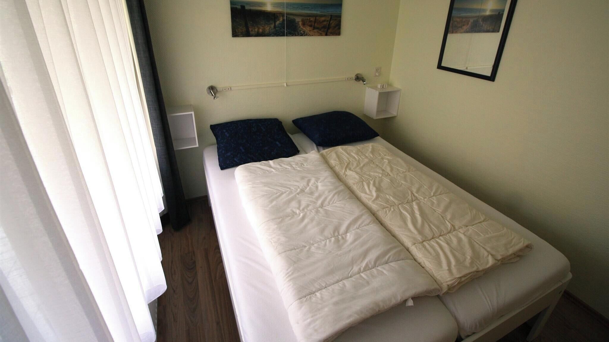 Un lit simple avec une couette, deux oreillers, une table de chevet, une lampe fixée au mur et un tableau.