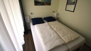 Un letto singolo con una coperta, due cuscini, un comodino, una lampada a parete e un quadro.
