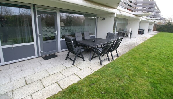 A patio with a table and chairs, a sliding glass door, and a grassy lawn.