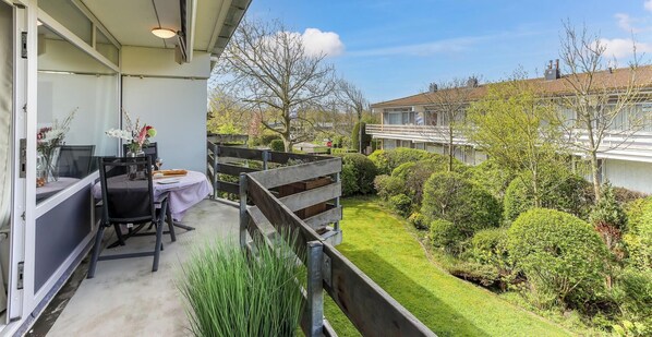 A balcony with a table and chairs, a view of a green garden, and a neighboring building. - Comfort Vikingpark 16 (Westkapelle)