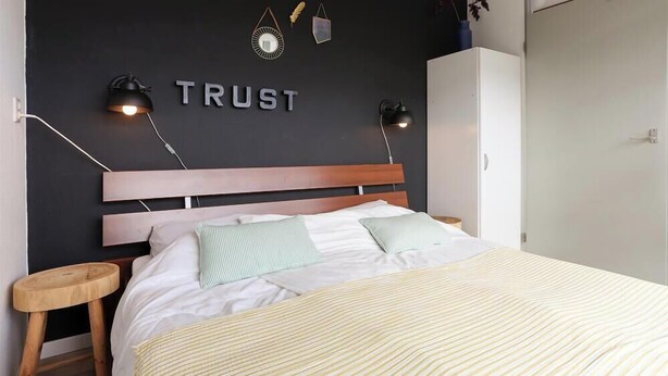 Une chambre à coucher comprenant un lit, des tables de chevet, une armoire et un mur sur lequel est inscrit le mot «CONFIANCE» au-dessus du lit.