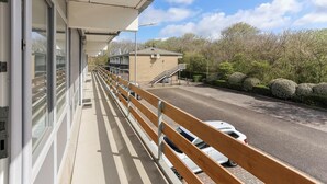 Un balcon donnant sur une rue, une voiture garée et un immeuble avec un escalier.