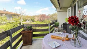 Un balcon avec une table dressée pour le dîner, un vase rempli de fleurs et une vue sur un quartier résidentiel.