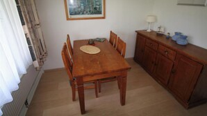 A dining area with a wooden table and chairs, a small cabinet with a lamp, and a framed picture on the wall.