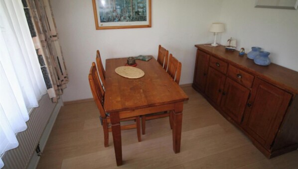 A dining area with a wooden table and chairs, a small cabinet with a lamp, and a framed picture on the wall. - Comfort Vikingpark 51 (Westkapelle)